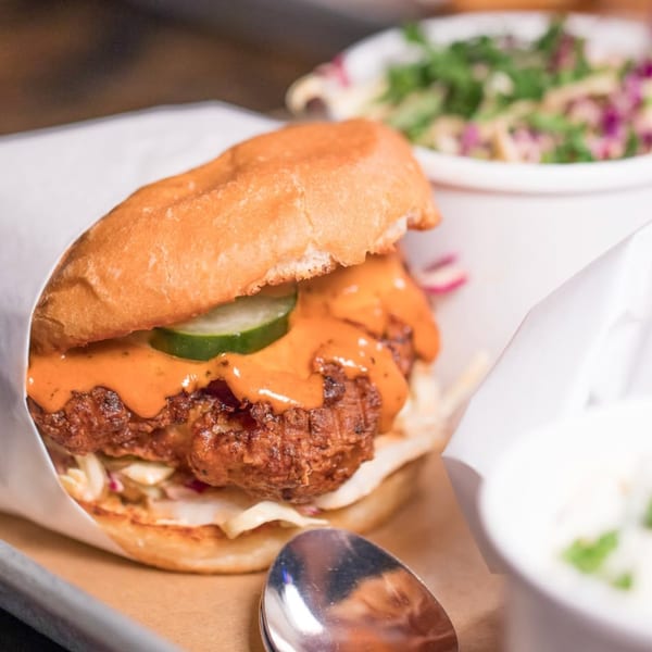 A Cross-Eyed Cricket fried chicken sandwich with sauce and pickles, served with coleslaw.