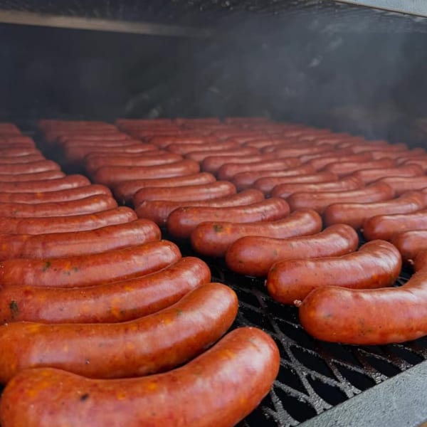Numerous rows of smoked sausages cooking on a grill with visible smoke at The Cross-Eyed Cricket.